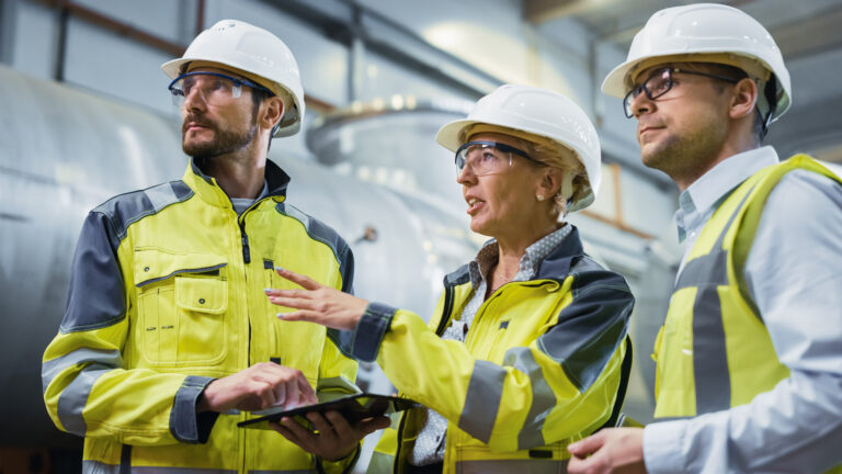 Three Heavy Industry Engineers Stand in Pipe Manufacturing Facto