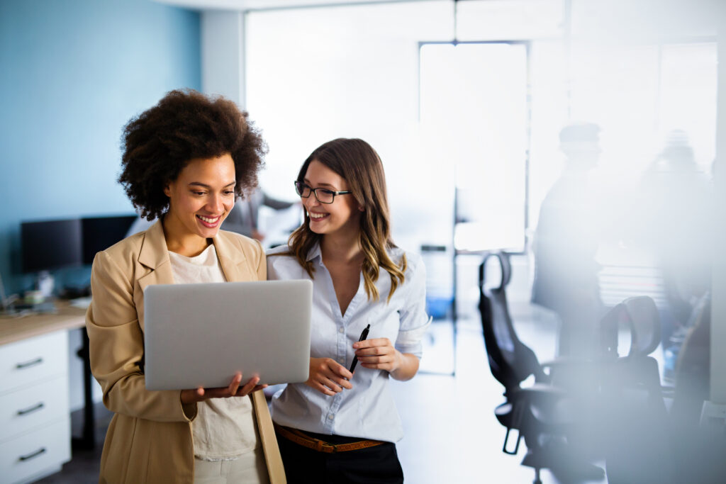 Happy multiethnic business women working together online on a laptop in corporate office.